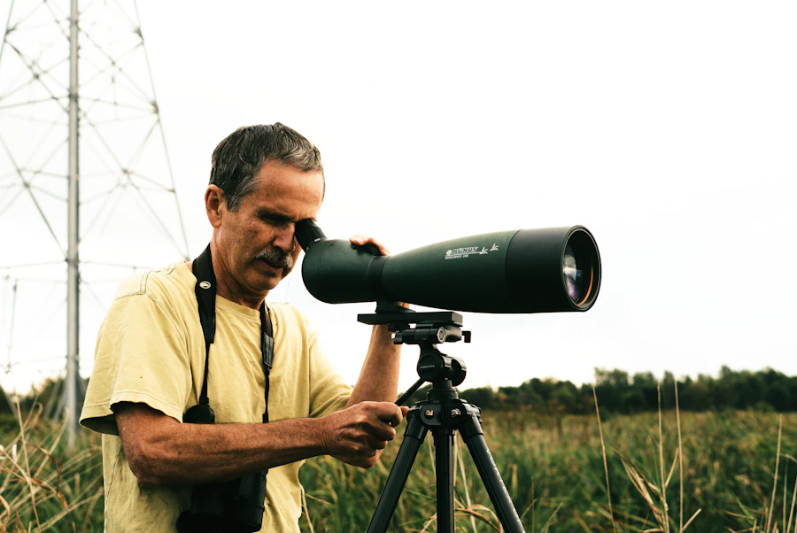 Man looking through a spotting scope mounted on a tripod in a field